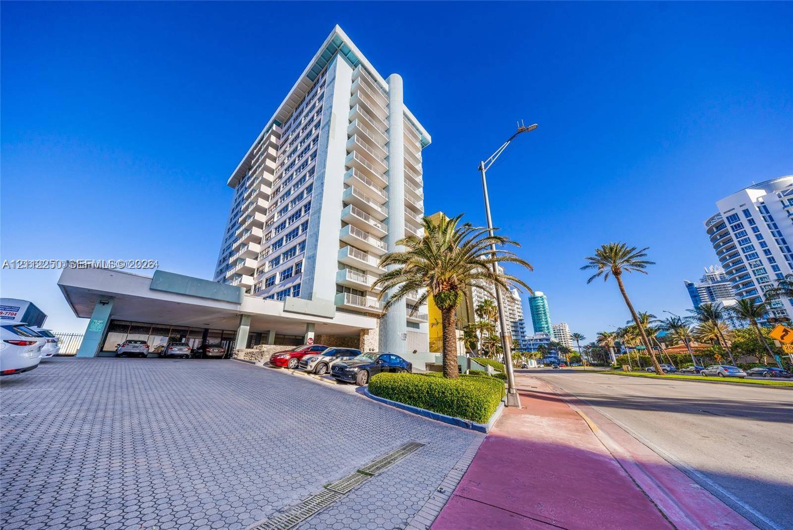 High-rise residential building featuring a covered portico entry, paved driveway, multi-level balconies, and exterior landscape plantings