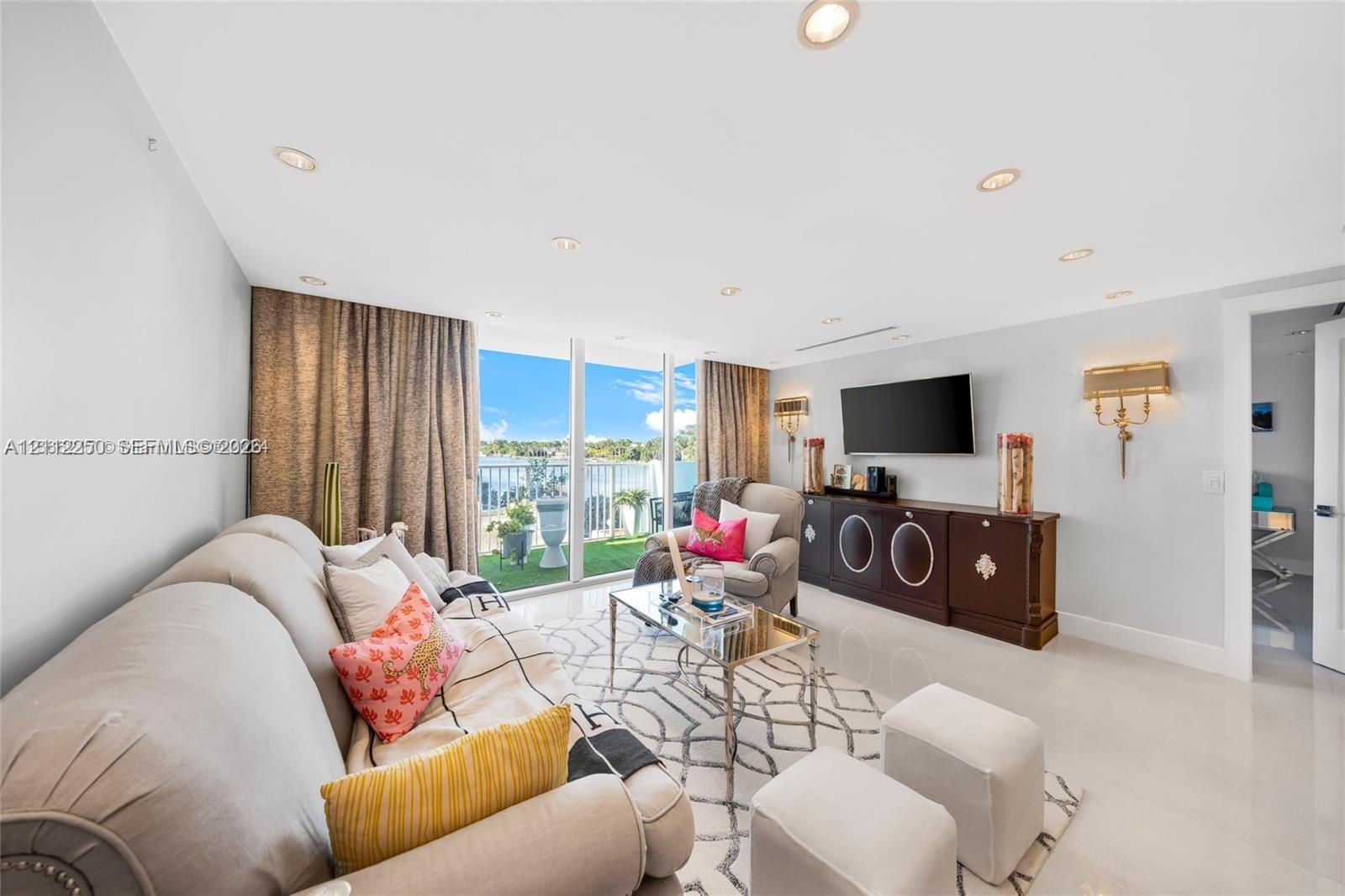 Living area featuring recessed lighting, large-format tile flooring, wall-mounted light fixtures, and floor-to-ceiling glass doors opening to a balcony