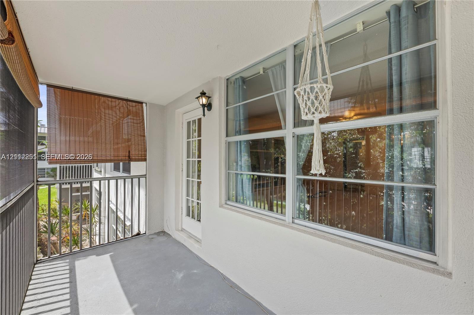 Covered balcony featuring metal railings, a full-lite glass panel door, exterior wall-mounted lighting, and neutral flooring