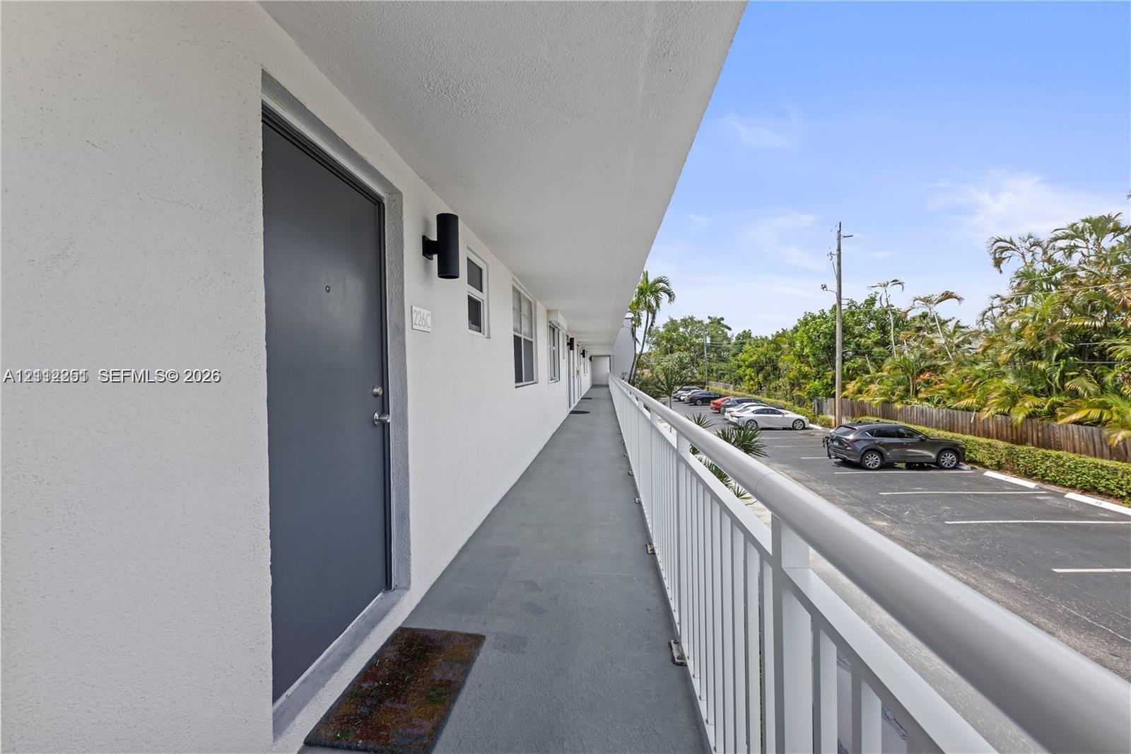 Exterior walkway featuring a painted solid-core door, cylindrical wall-mounted sconce lighting, and a white metal safety railing
