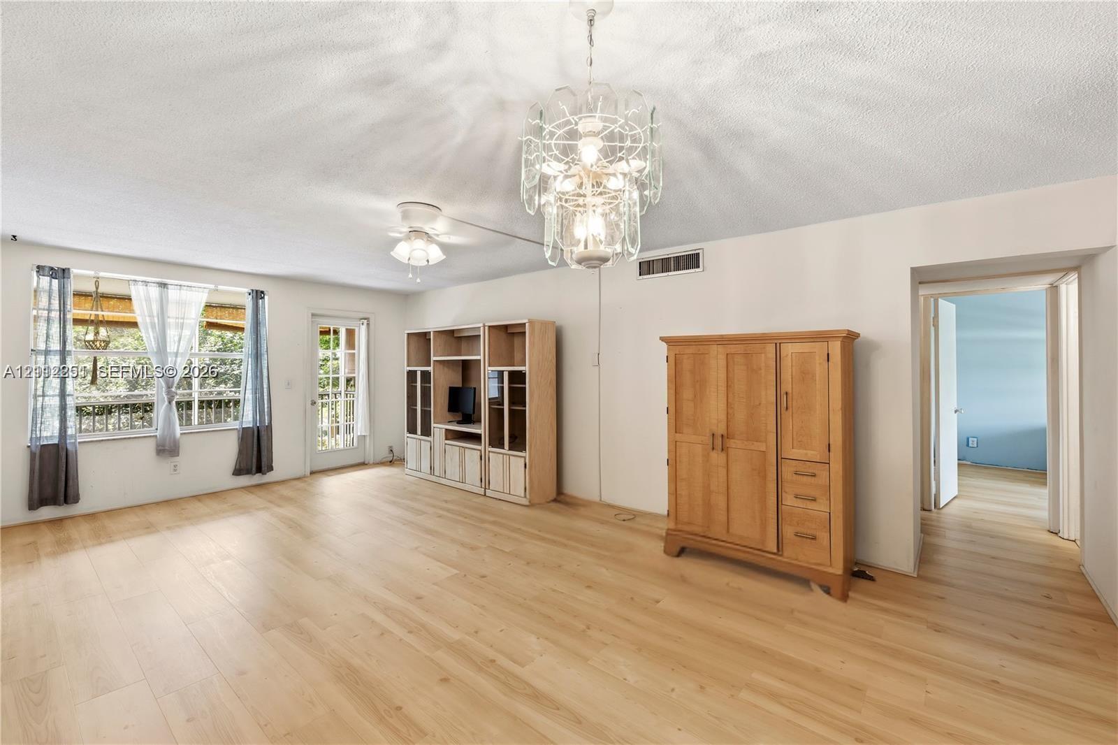 Open floor plan featuring wood-finish flooring, a multi-tiered crystal chandelier, a ceiling fan with integrated lighting, and built-in floor-to-ceiling cabinetry Open floor plan featuring wood-finish flooring, a multi-tiered crystal chandelier, a ceiling fan with integrated lighting, and built-in floor-to-ceiling cabinetry