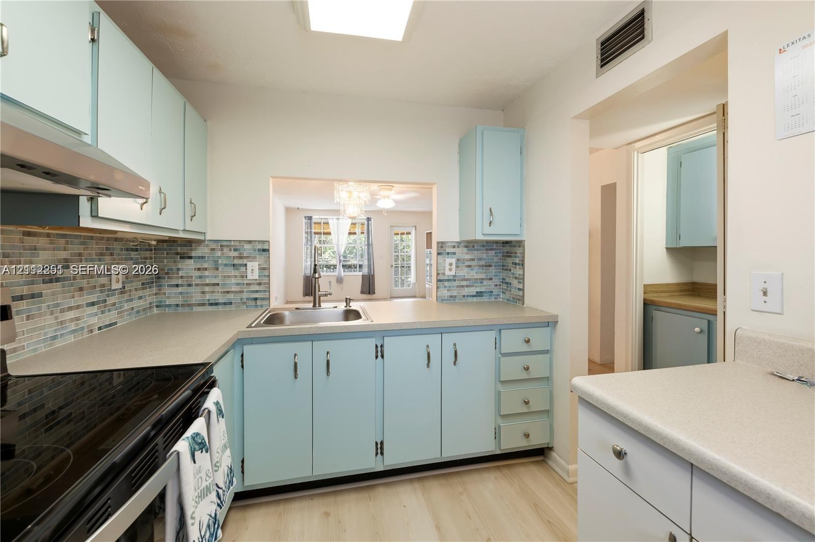 Kitchen featuring solid-surface countertops, custom light blue cabinetry, decorative glass tile backsplash, stainless steel sink, and wood-finish flooring