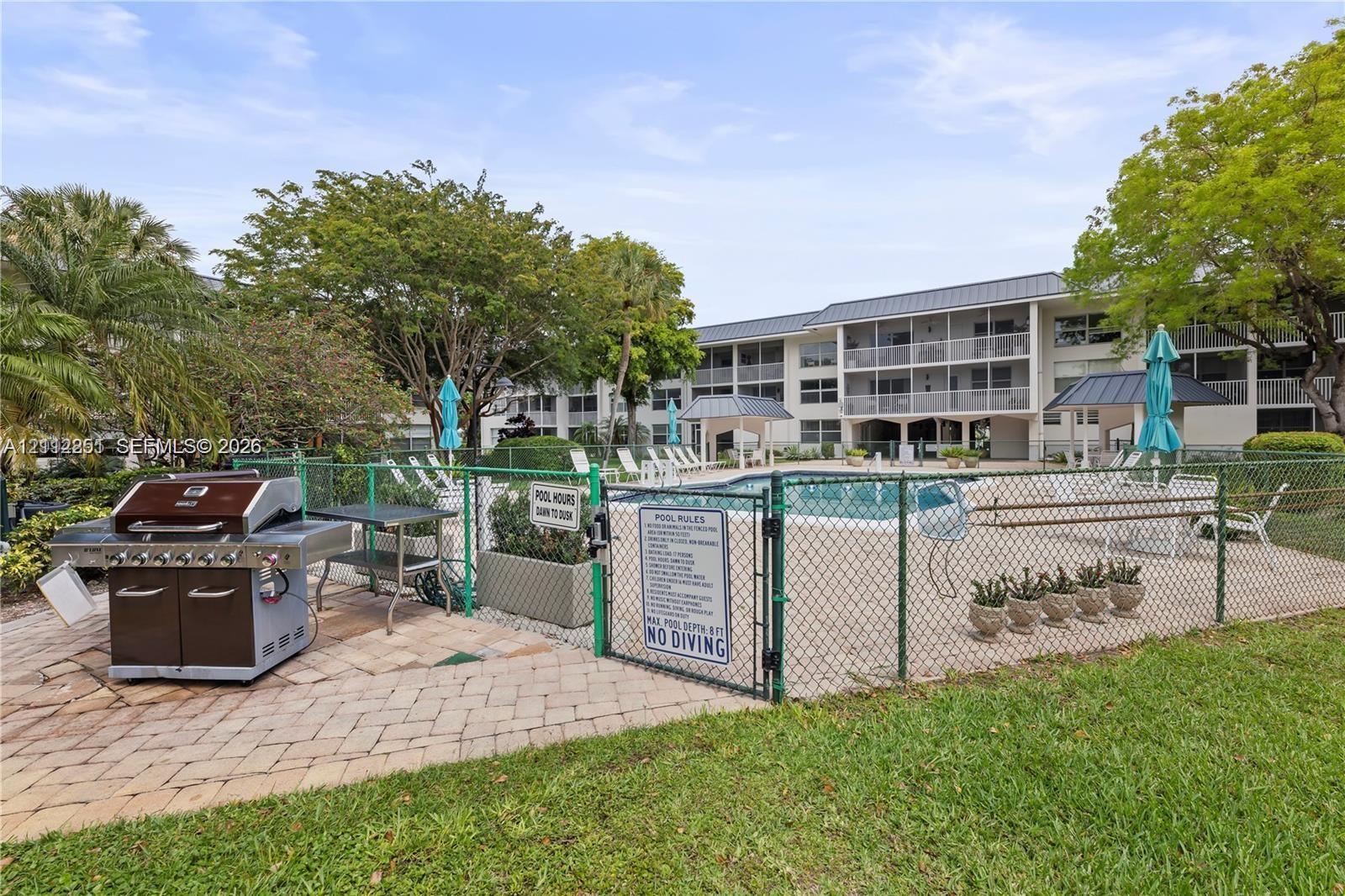 Community swimming pool with brick paver surround, built-in stainless steel outdoor grill station, and mature landscaping