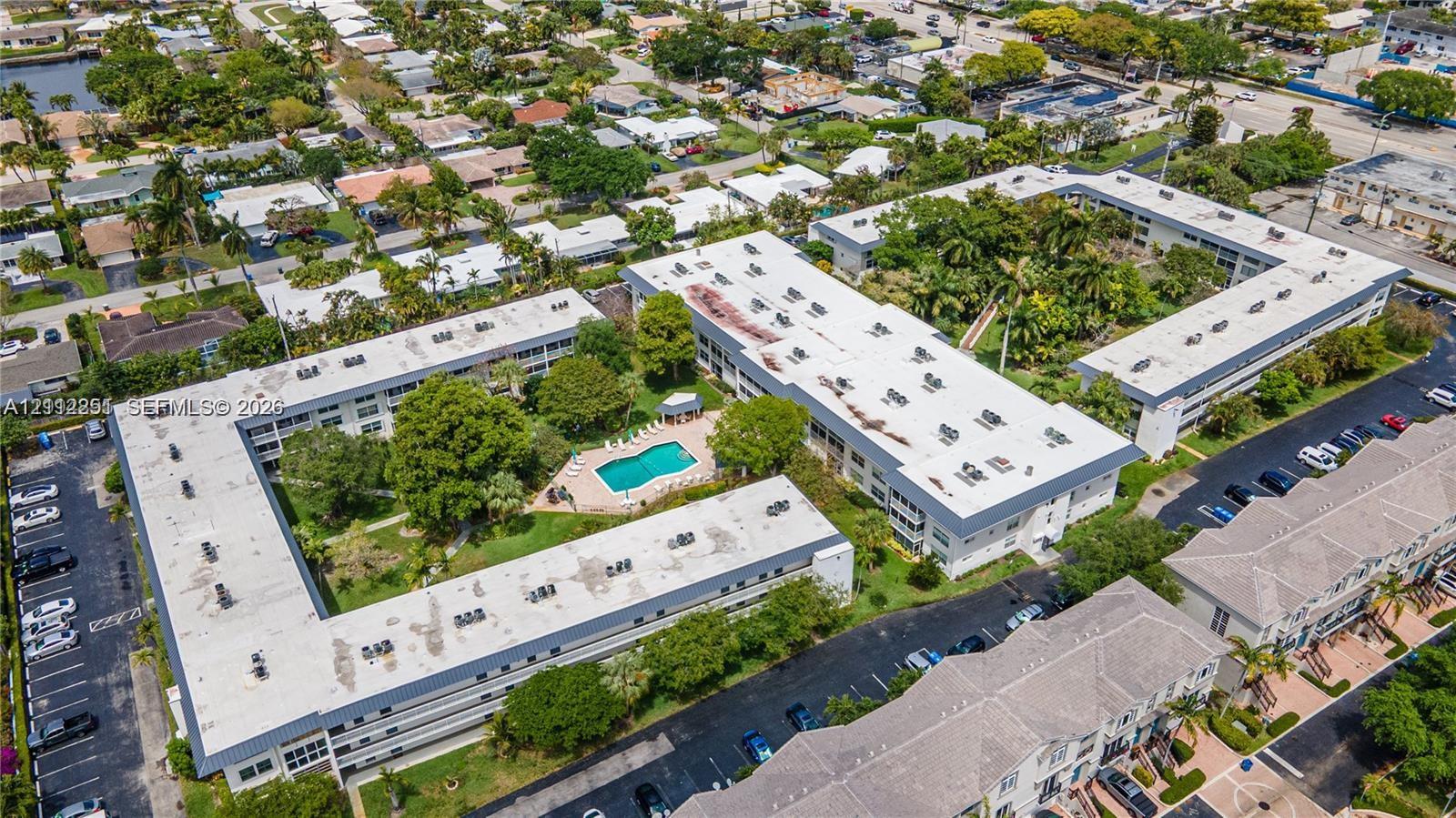 Aerial perspective of the property featuring a central swimming pool, paved surface parking areas, and mature landscaping
