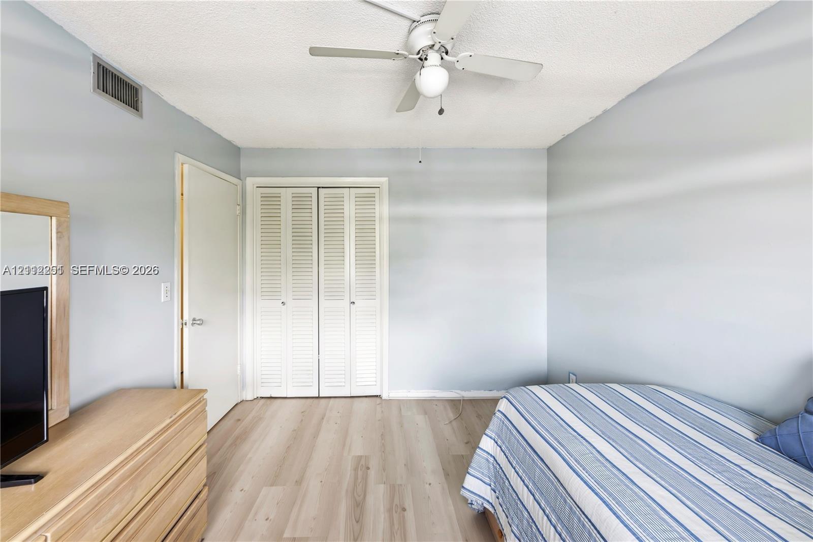 Room featuring wood-finish flooring, white louvered-style closet doors, and a ceiling-mounted light fixture with a central fan