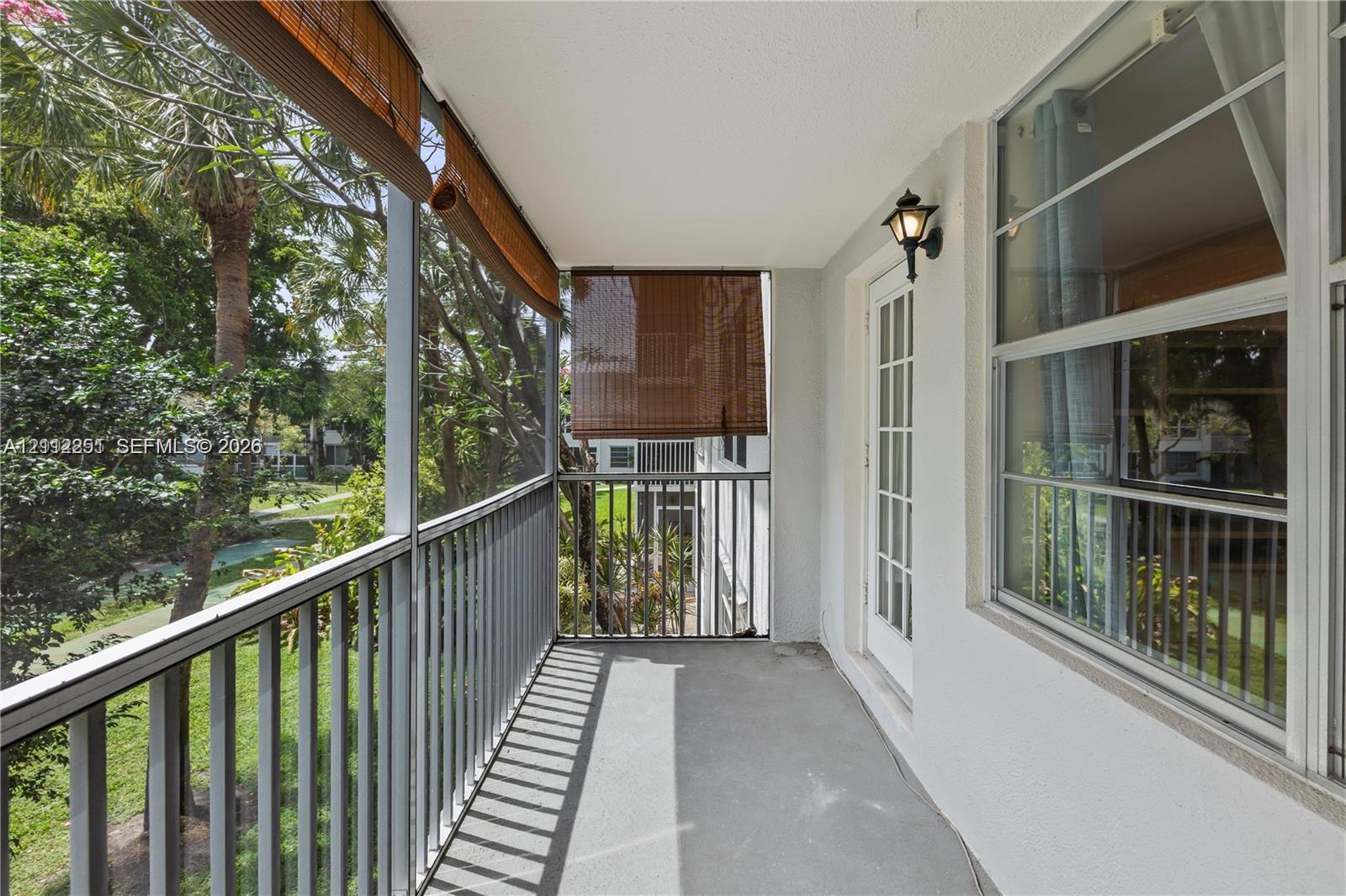Screened balcony featuring vertical metal railings, concrete flooring, exterior wall-mounted lighting, and a glass-paneled entry door