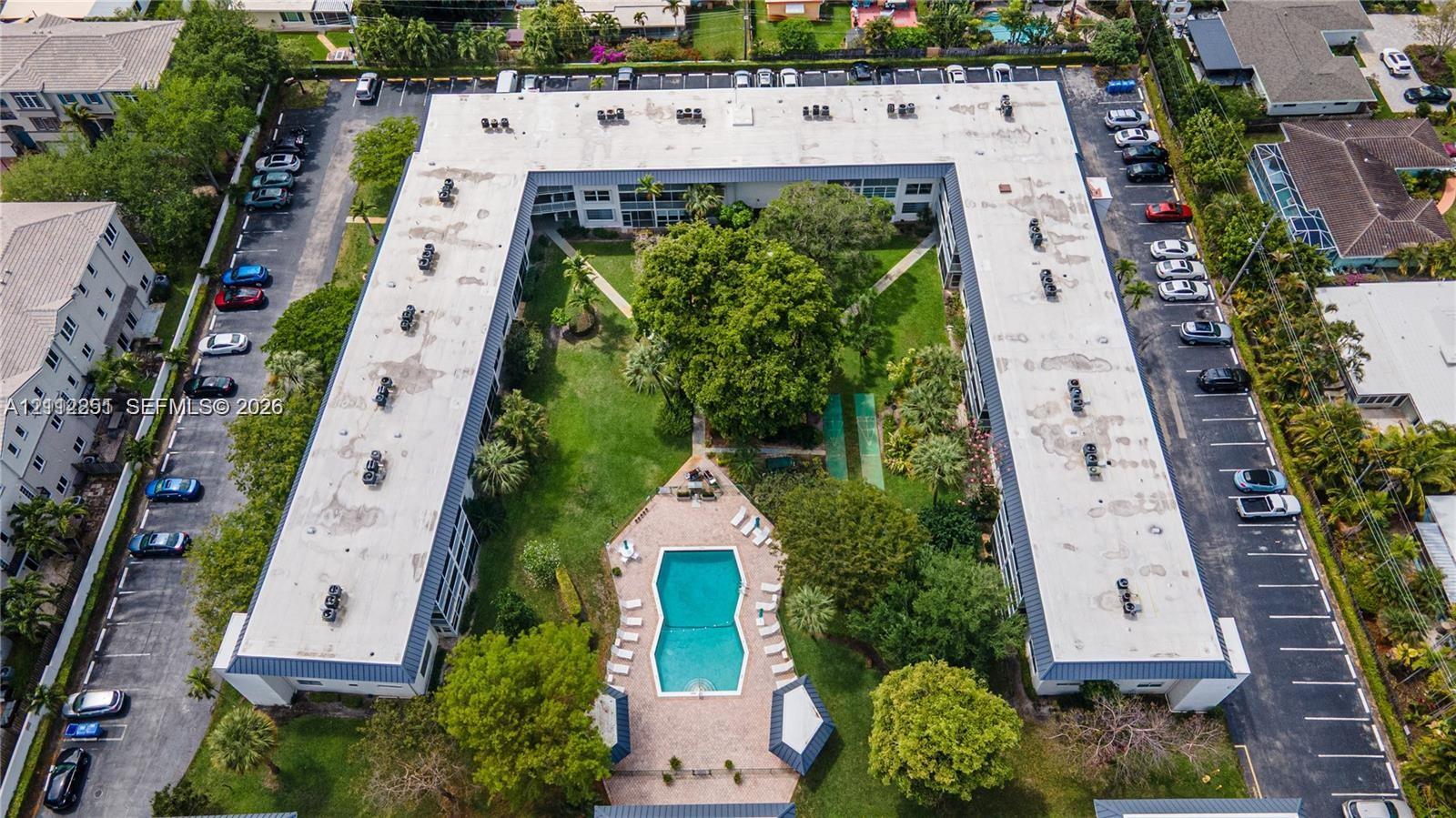 U-shaped residential complex featuring a central courtyard with a swimming pool, paver deck, mature landscaping, and dedicated surface parking