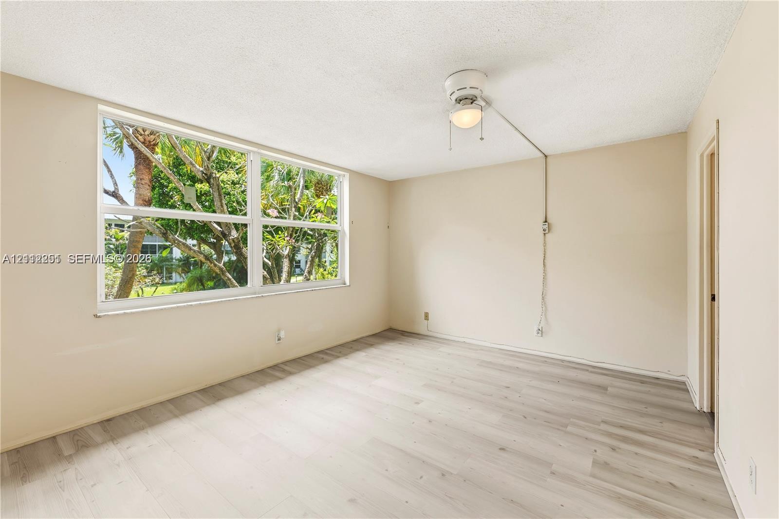 Room with wood-finish flooring, neutral walls, large window with natural light, and ceiling fan with integrated light fixture Room with wood-finish flooring, neutral walls, large window with natural light, and ceiling fan with integrated light fixture