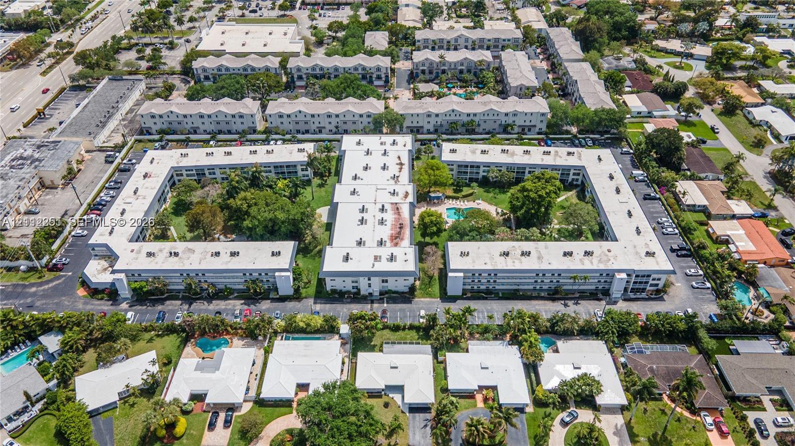 Aerial perspective of a multi-building residential complex featuring a central courtyard, landscaped grounds, swimming pool, and dedicated asphalt parking areas