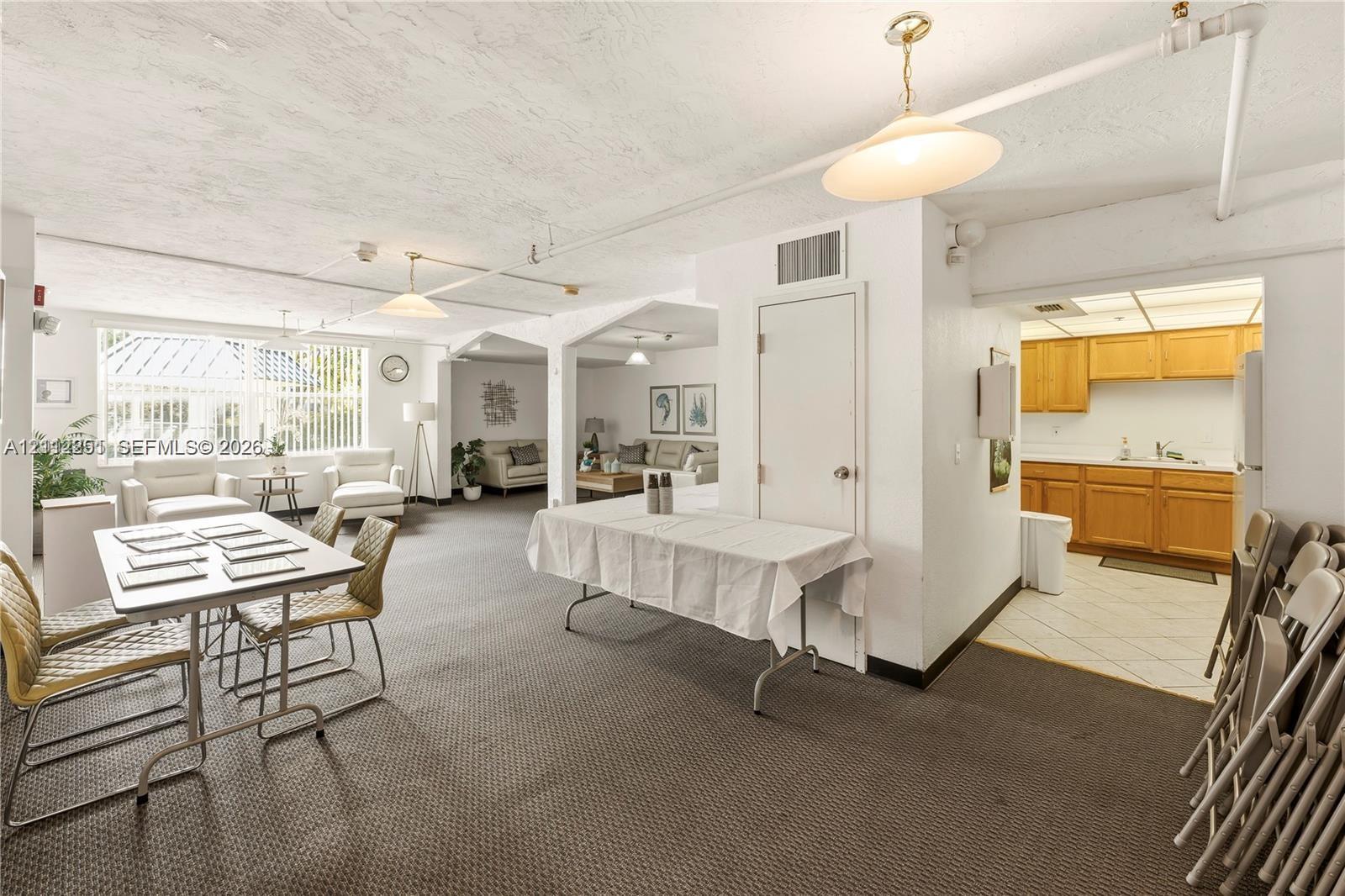 Open-concept interior featuring large windows, neutral carpeting, recessed and pendant lighting, and a kitchen area with wood-finish cabinetry