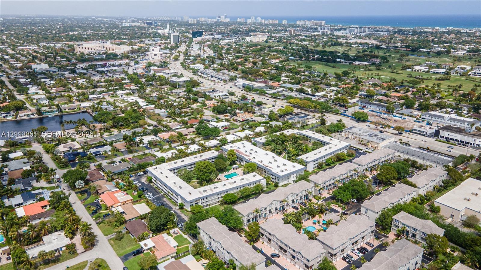 Aerial perspective of a multi-building residential complex featuring courtyards, swimming pools, and mature landscaping, situated within a coastal urban environment
