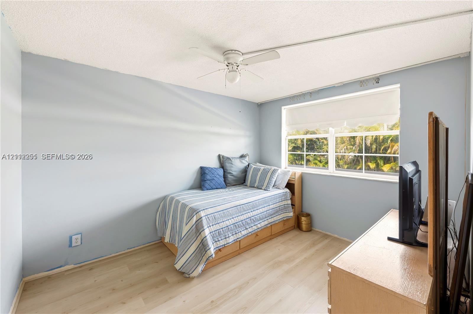 Room featuring wood-finish flooring, a multi-pane window, and a ceiling-mounted fan with integrated lighting