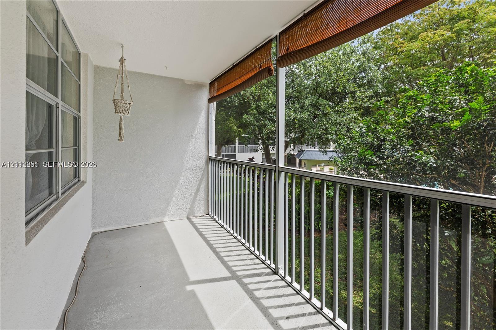 Screened-in balcony featuring concrete flooring, metal railing, and roll-down sun shades