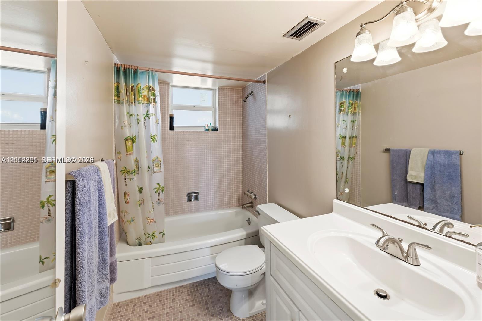 Bathroom featuring a white vanity with an integrated sink, a large wall-mounted mirror, a tub-shower combination with tile surround, and a tile-finished floor