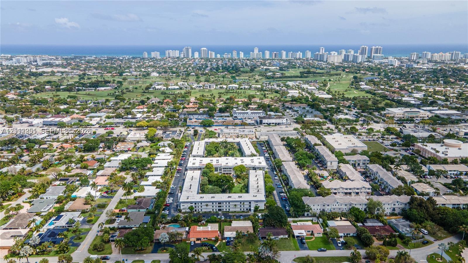 Aerial perspective of a multi-story residential complex featuring a central courtyard with mature landscaping and proximity to the coastline