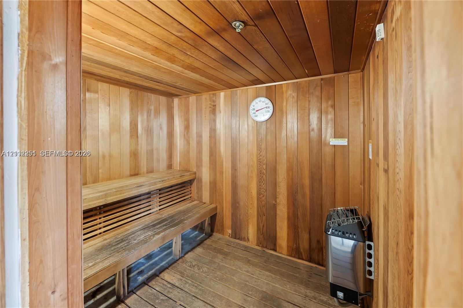 Sauna featuring wood-plank walls and ceiling, slatted wood bench seating, and an integrated heating unit