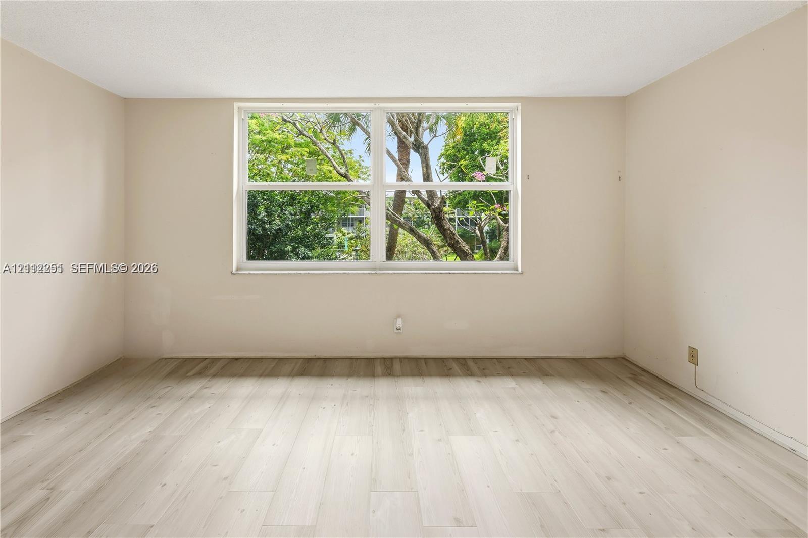 Room featuring wood-finish flooring, neutral-toned walls, and a large horizontal window with exterior greenery