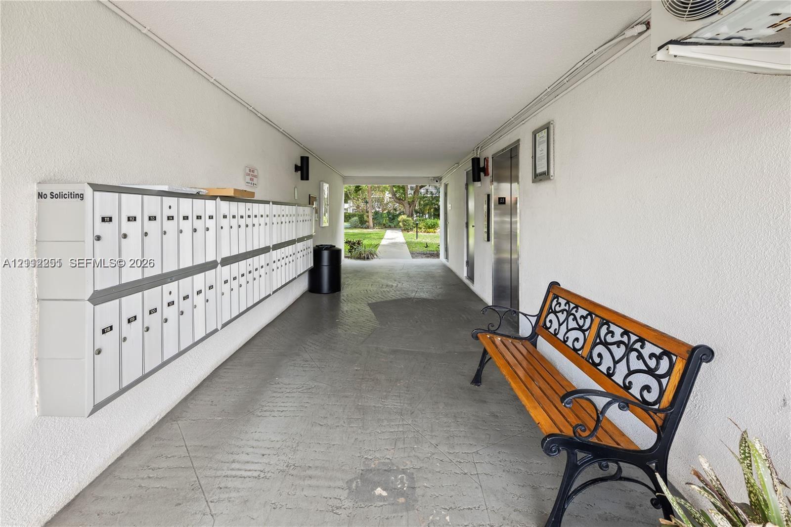 Covered breezeway featuring a wall-mounted communal mailbox bank, metallic elevator doors, and textured wall finishes
