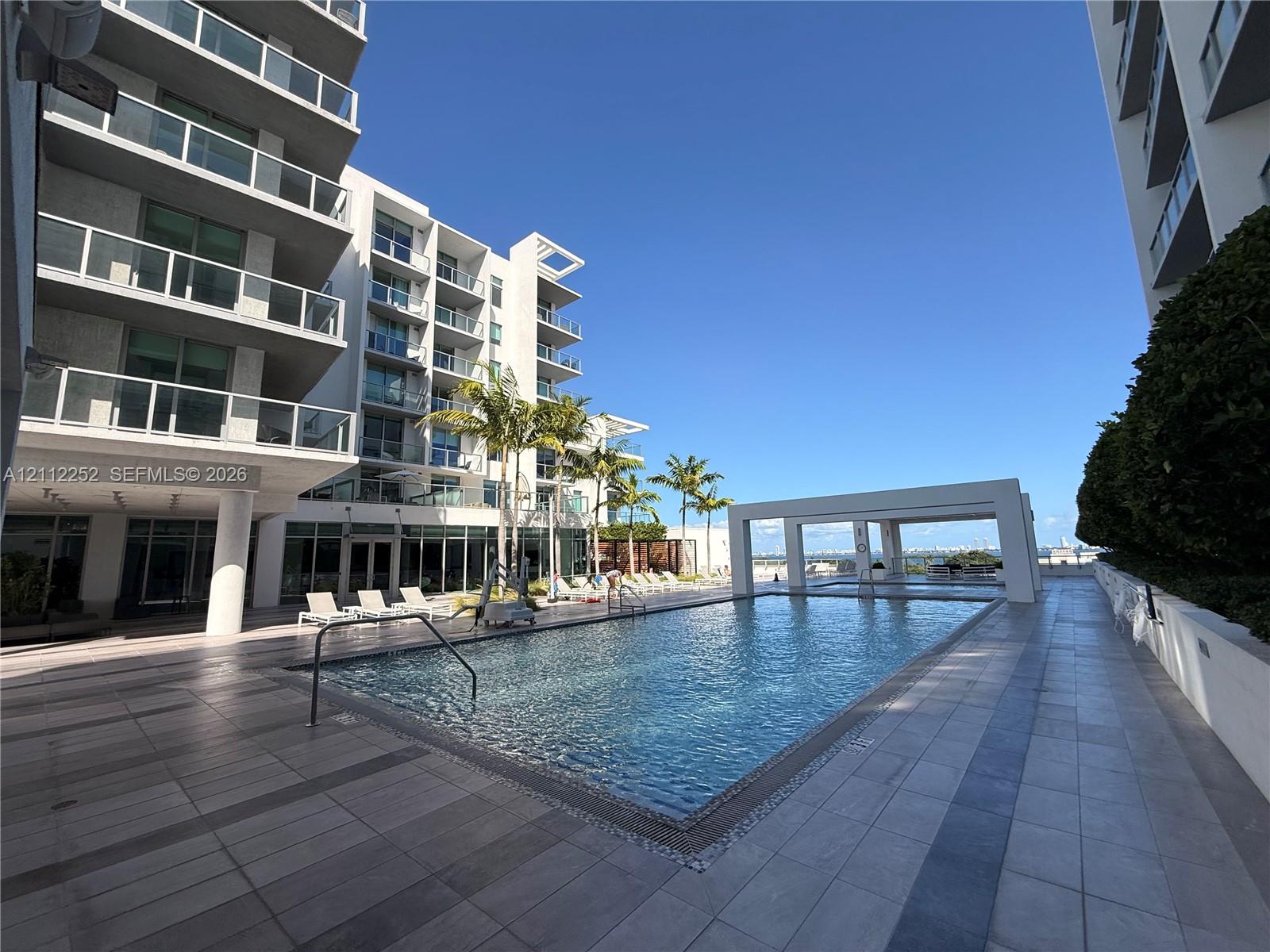 Swimming pool with tiled decking, poolside cabana, and multi-story architectural exterior featuring glass-paneled balconies