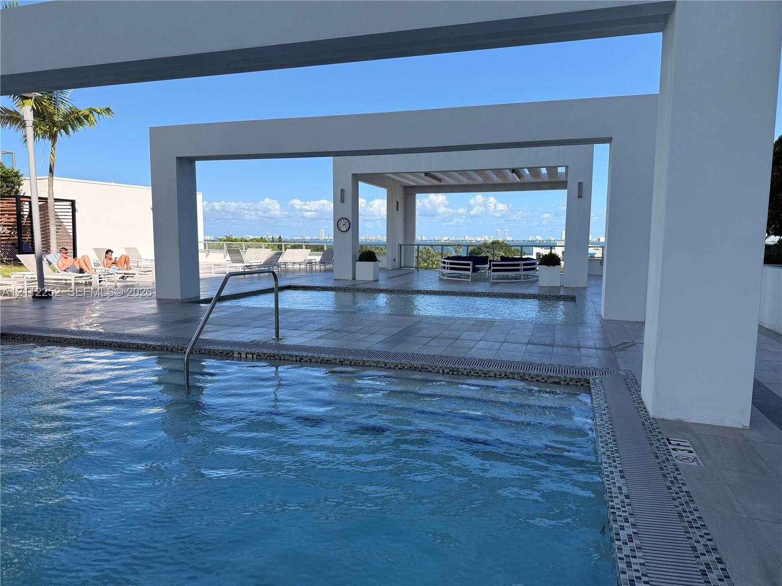 Swimming pool with metal handrail, tiled deck, and geometric overhead structures