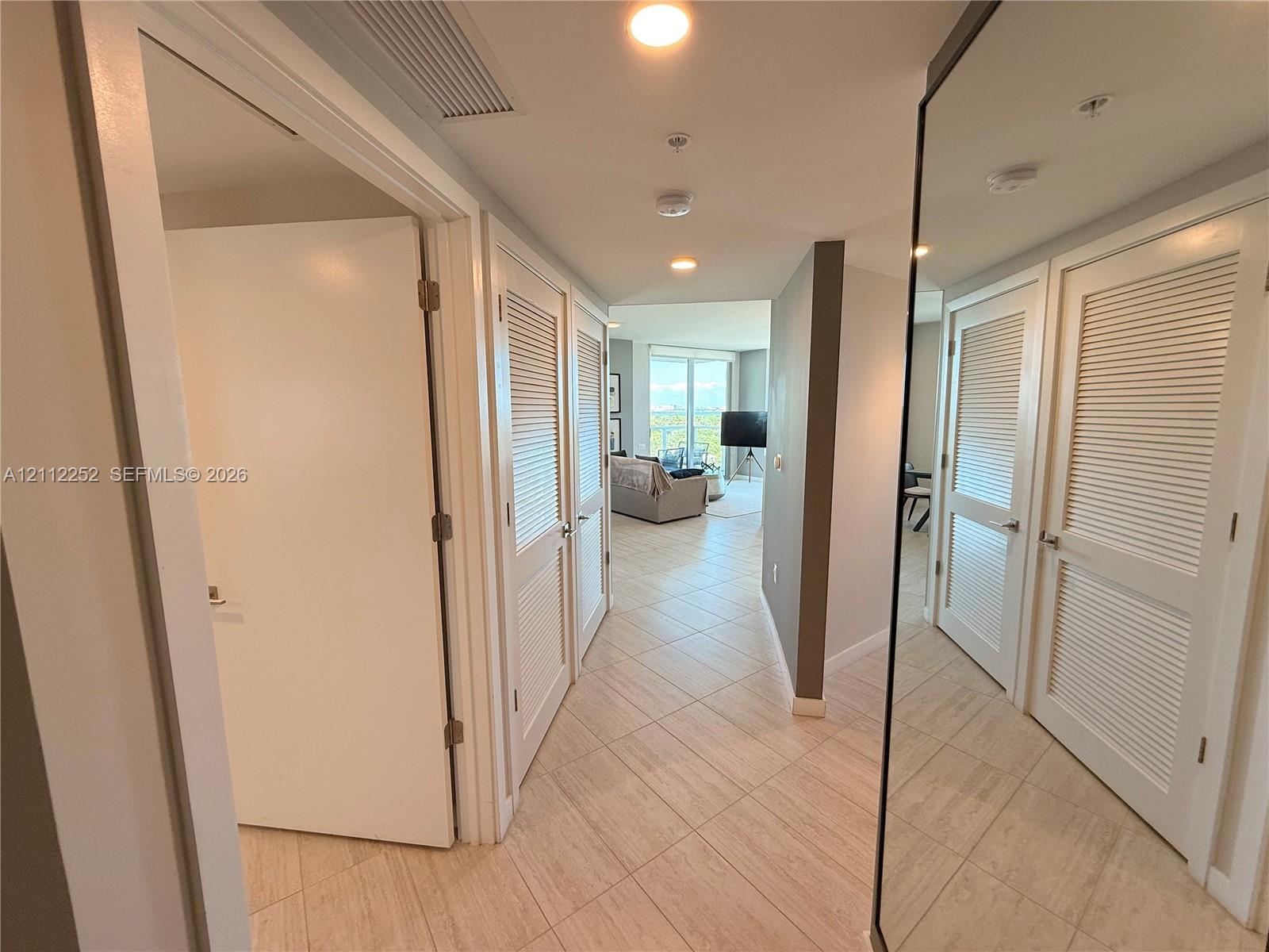 Hallway featuring large-format tile flooring, recessed ceiling lighting, louvered-panel closet doors, and a full-length mirrored door