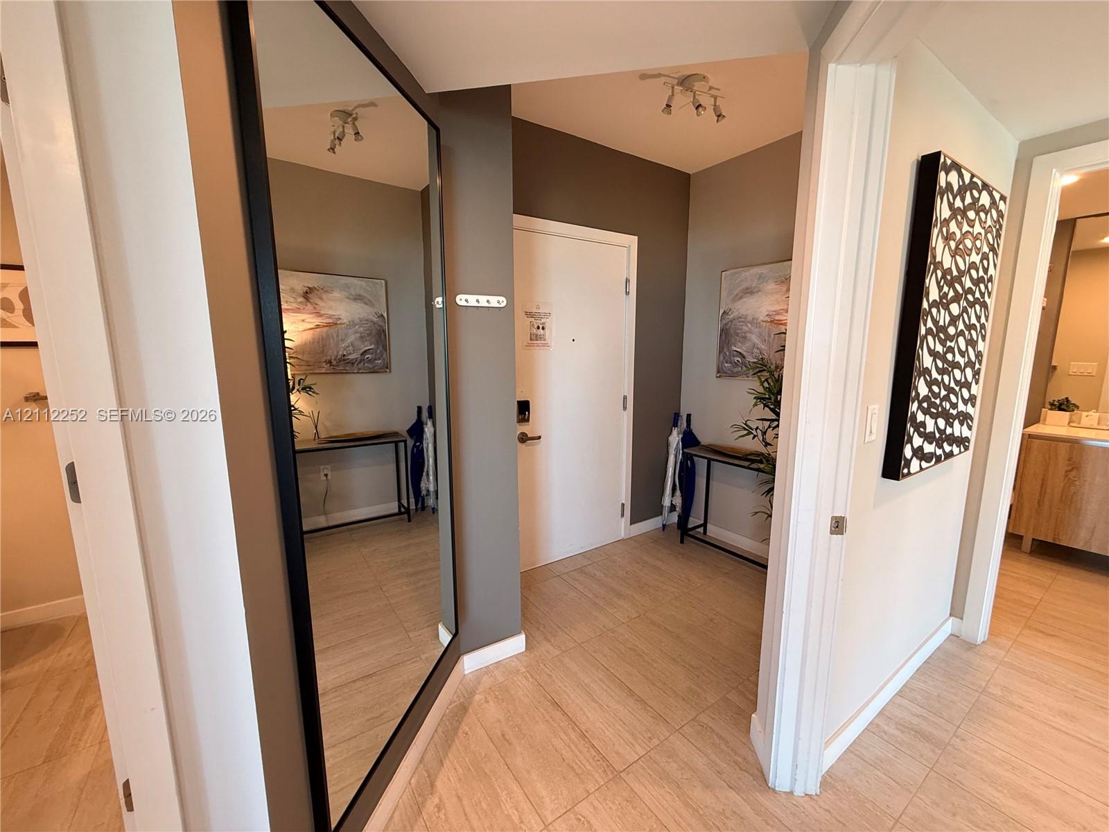 Entryway featuring large-format tile flooring, a floor-to-ceiling wall-mounted mirror with a black frame, and multi-directional overhead track lighting