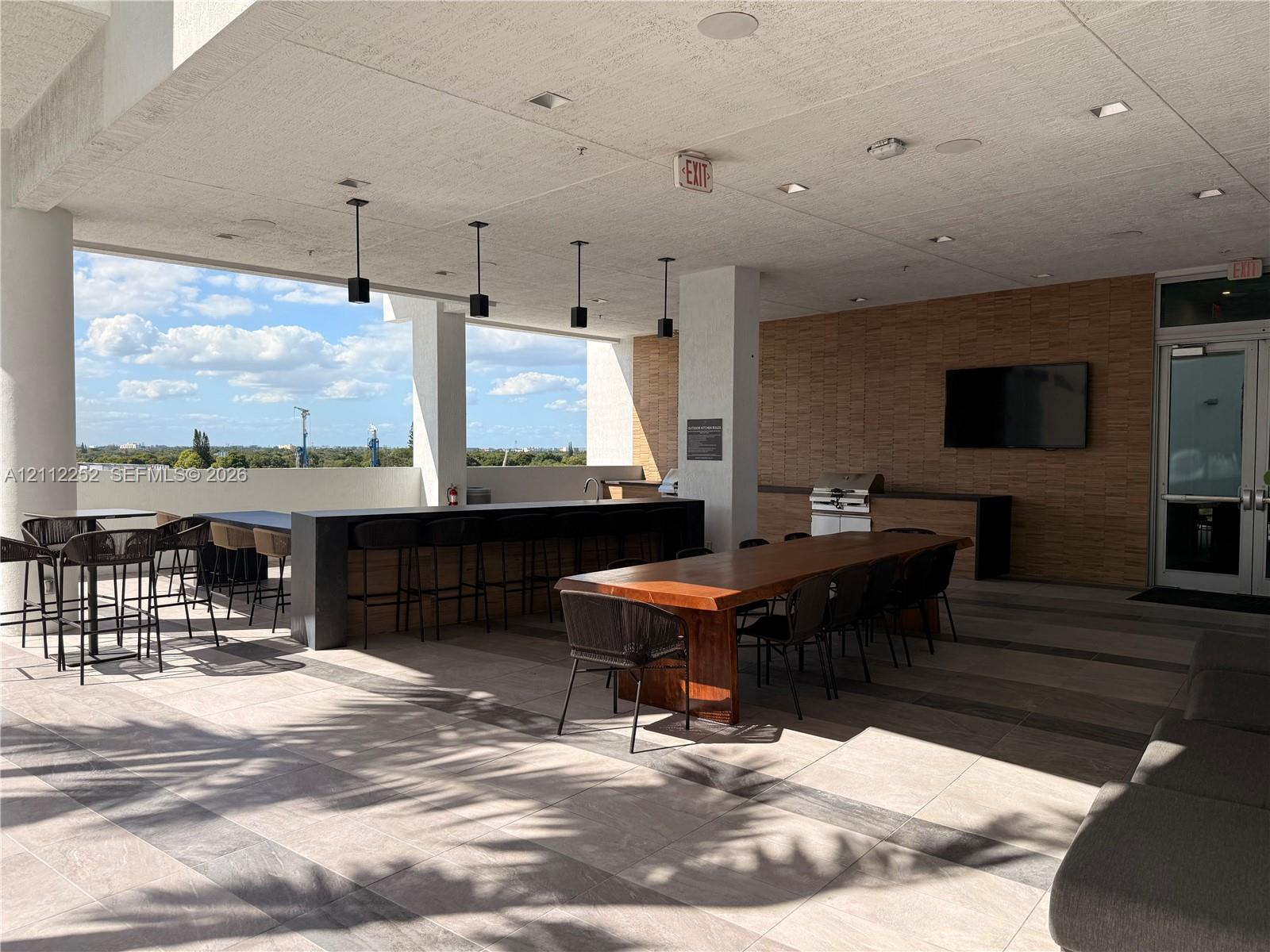 Covered rooftop terrace featuring large-format tile flooring, a built-in outdoor kitchen with stainless steel grill, a stone-tiled accent wall, and recessed ceiling lighting