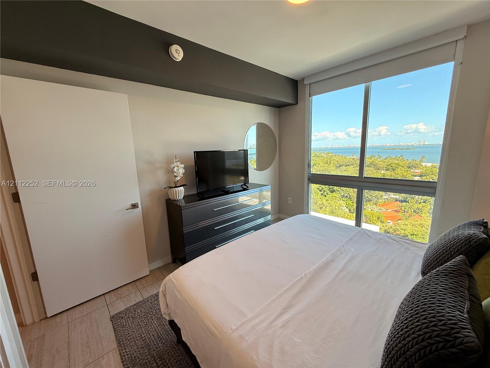Floor-to-ceiling windows featuring expansive coastal and woodland scenery, tile flooring, and solid-core door