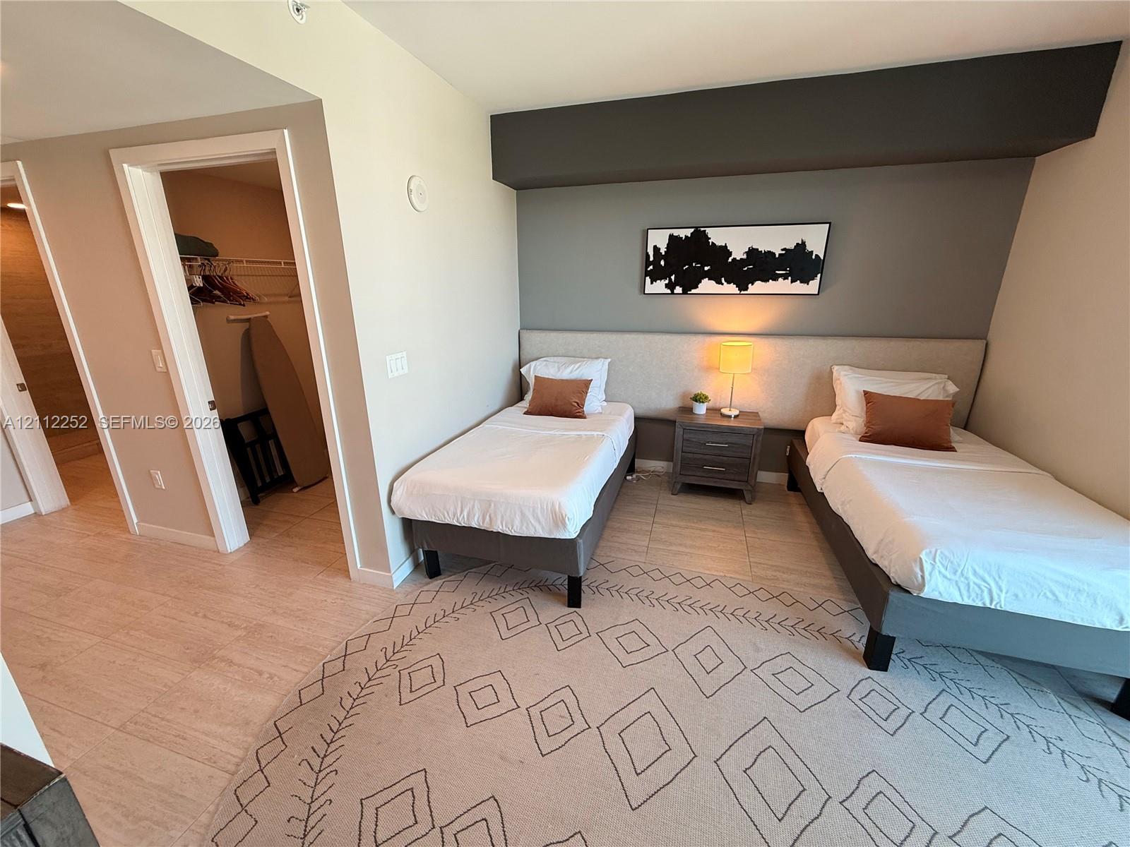 Neutral-toned interior featuring continuous light-colored flooring, a custom upholstered headboard wall, an accent wall with architectural bulkhead, and an open-entry reach-in closet with wire shelving