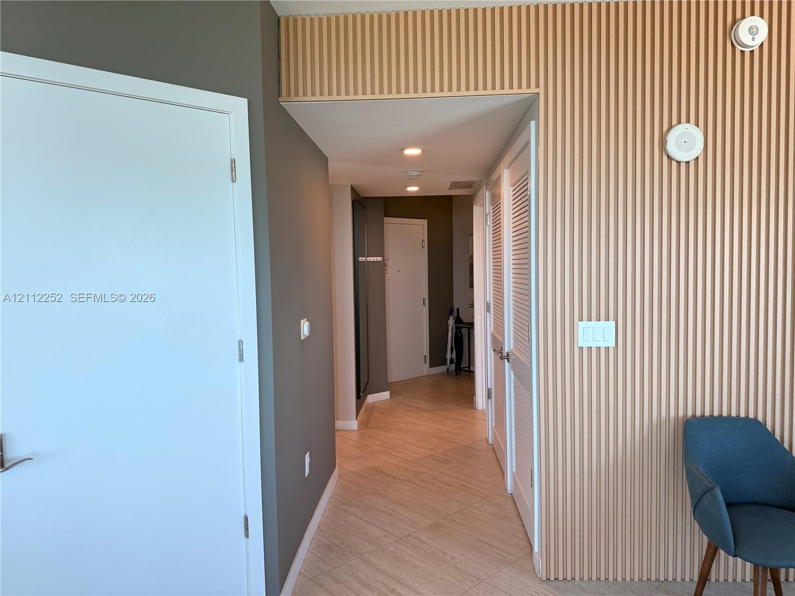 Vertical wood-slat wall paneling, tile flooring, recessed ceiling lighting, and louvered closet doors