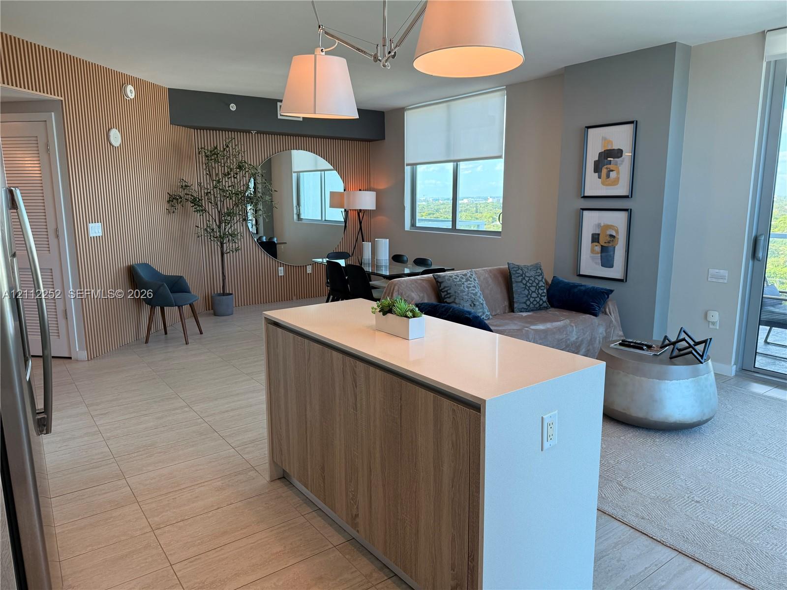 Kitchen island featuring a stone countertop and wood-finish cabinetry, accent wall with vertical fluting, large circular wall-mounted mirror, and tile flooring