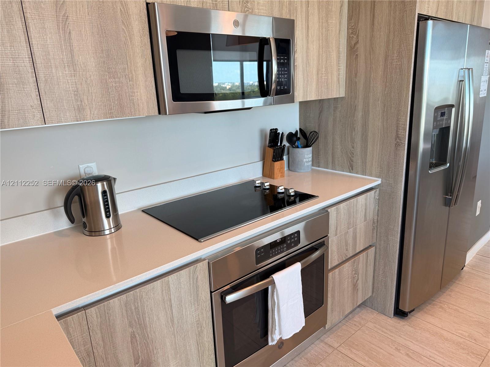 Kitchen featuring flat-panel wood-finish cabinetry, quartz countertops, stainless steel appliances, a smooth-surface electric cooktop, and built-in microwave