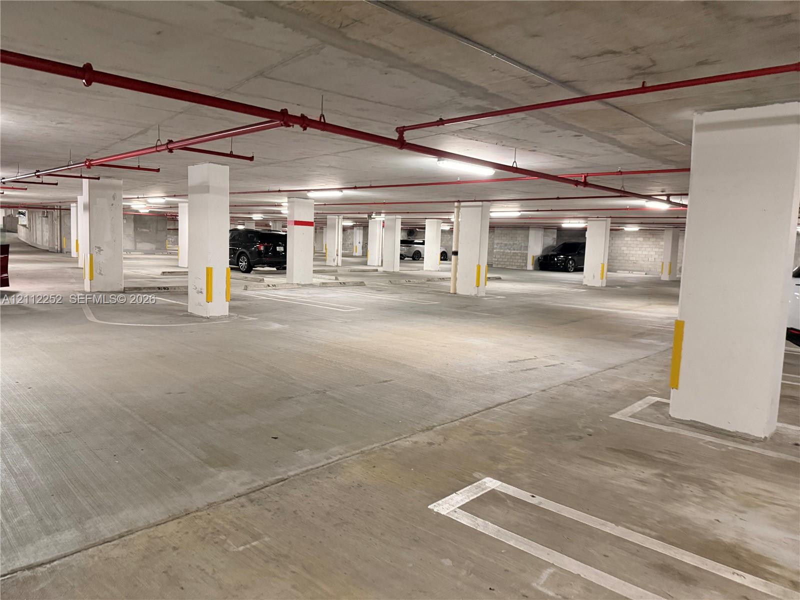 Covered parking garage with a concrete floor, concrete support columns, and overhead sprinkler system