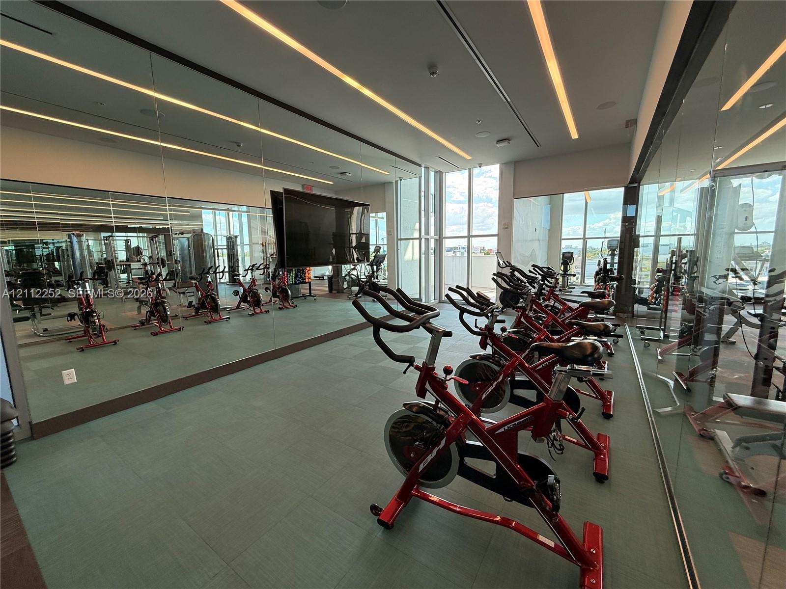 Fitness center featuring floor-to-ceiling mirrors, large-format tile flooring, linear recessed lighting, and extensive windows