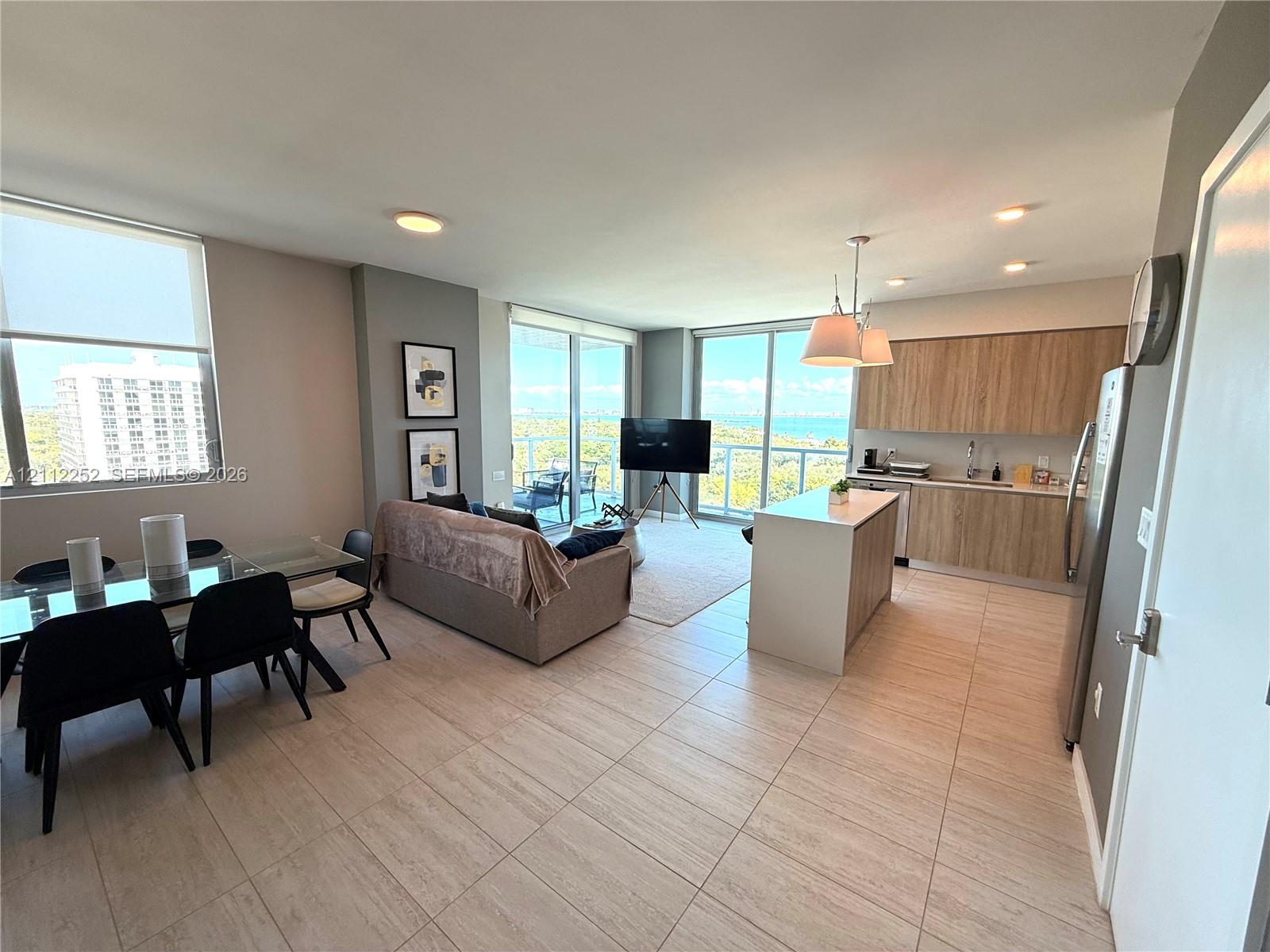 Open-concept living space featuring wood-finish cabinetry, a kitchen island, floor-to-ceiling glass windows, and ceramic tile flooring