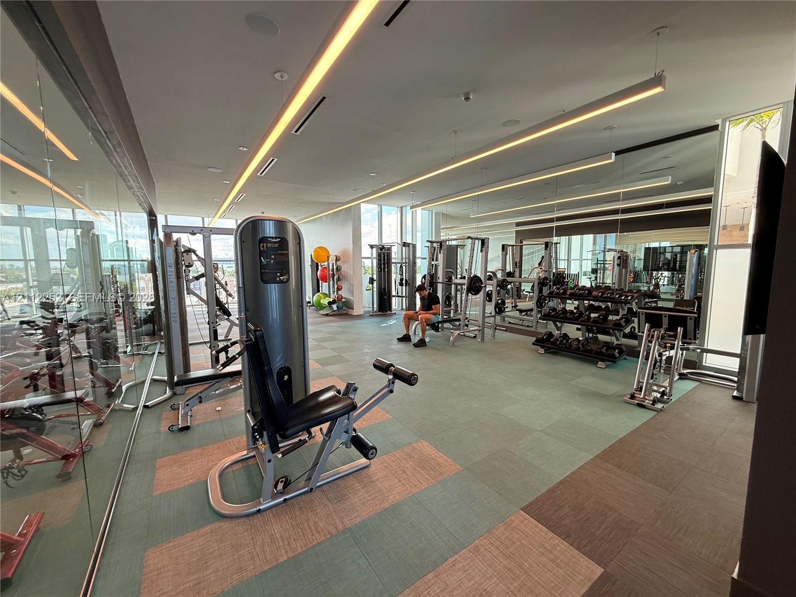 Fitness center featuring wall-to-wall mirrors, recessed linear LED lighting, floor-to-ceiling glass windows, and modular tile flooring