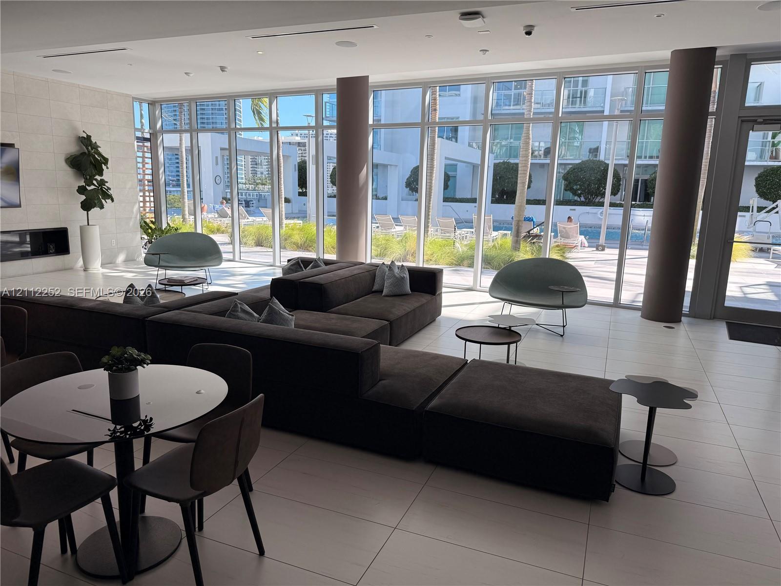 Common area featuring floor-to-ceiling windows, large-format tile flooring, built-in horizontal fireplace, and cylindrical support columns