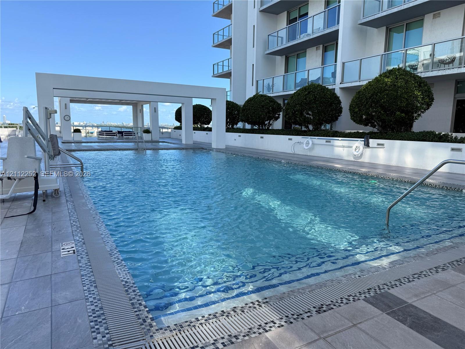 Outdoor swimming pool featuring a tiled deck, covered pavilion, manicured landscaping, and stainless steel handrails