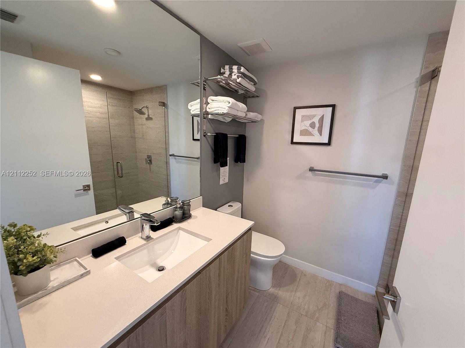 Bathroom featuring a vanity with a light-toned countertop, integrated basin, wood-finish cabinetry, floor-to-ceiling mirror, and a walk-in shower with horizontal-tiled walls and a glass enclosure