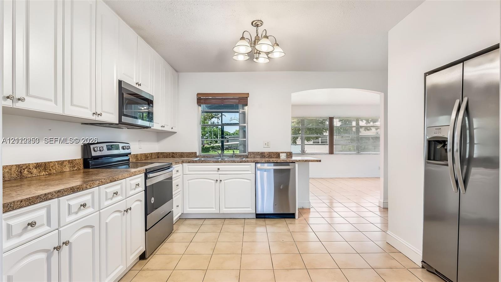 Kitchen featuring white cabinetry, stainless steel appliances, ceramic tile flooring, and a multi-light chandelier