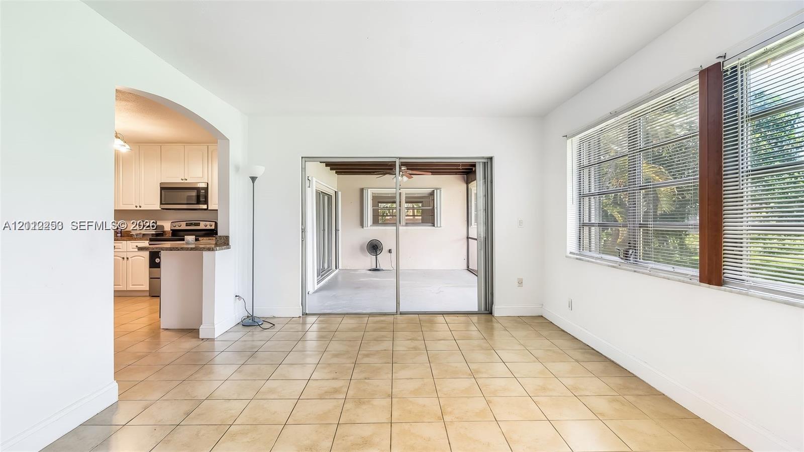 Ceramic tile flooring, arched wall opening, sliding glass doors, horizontal window blinds, and kitchen cabinetry with stone-finish countertops
