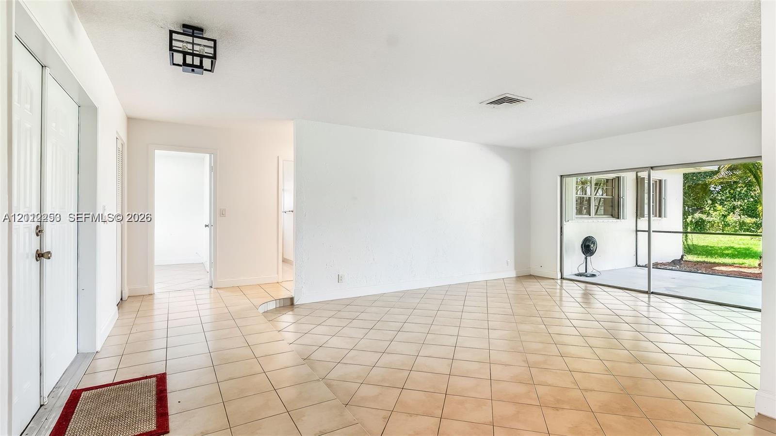 Open-concept interior featuring oversized tile flooring, a geometric matte black flush-mount light fixture, and sliding glass doors with exterior screen enclosure