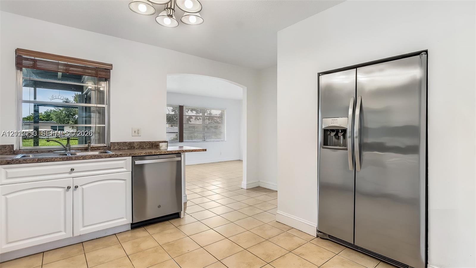 Kitchen featuring white cabinetry, stone-finish countertops, stainless steel appliances, ceramic tile flooring, and a multi-light fixture