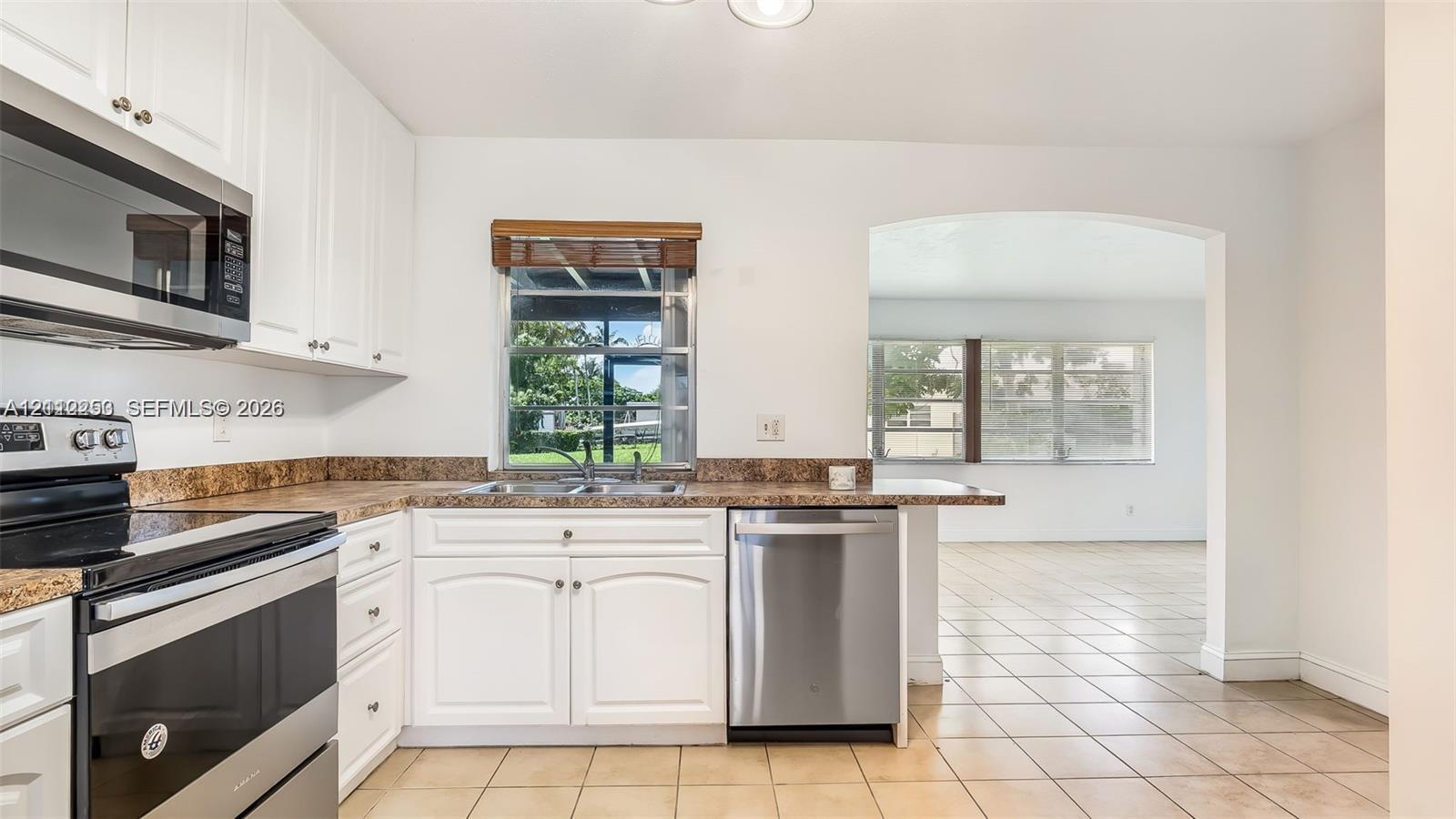 Kitchen featuring white cabinetry, stainless steel appliances, patterned laminate countertops, a double-basin sink, and tile flooring