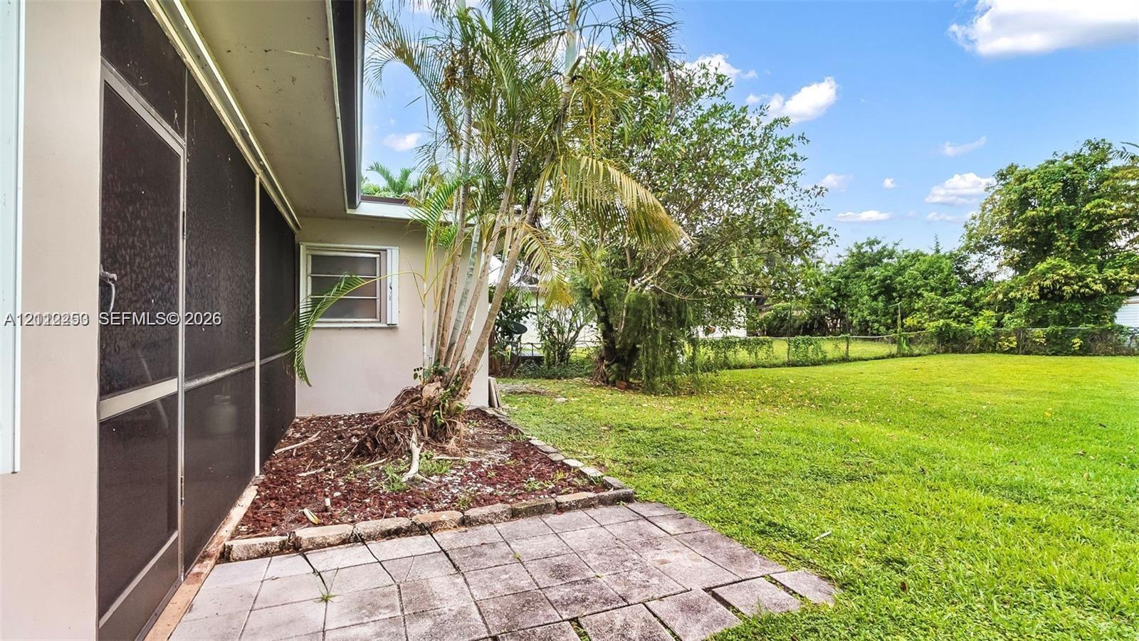 Screened-in exterior area featuring a concrete paver patio, mulched landscaping, mature palms, and an expansive lawn