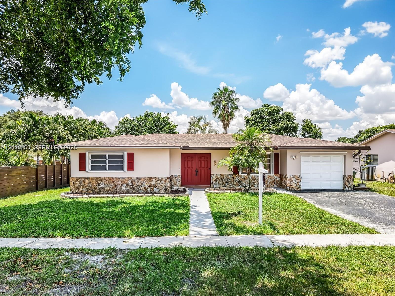 Single-story residence featuring a stone-veneer exterior, double-entry front doors, horizontal window shutters, a paved driveway, and an attached garage