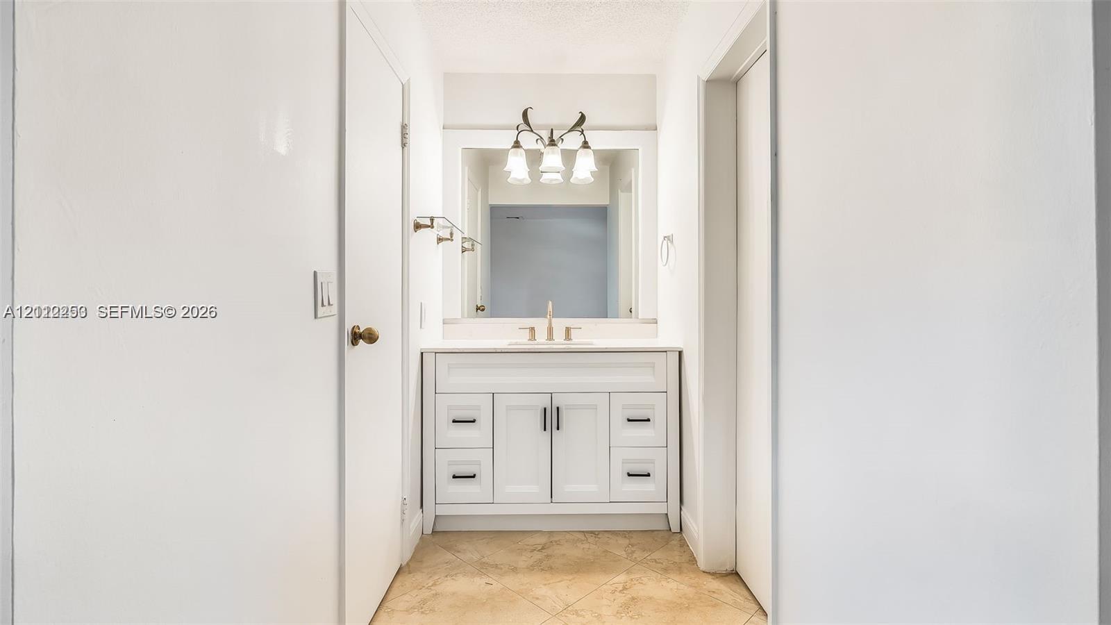 White shaker-style vanity with matte black hardware, integrated countertop with faucet, framed mirror, three-light vanity fixture, and neutral tile flooring