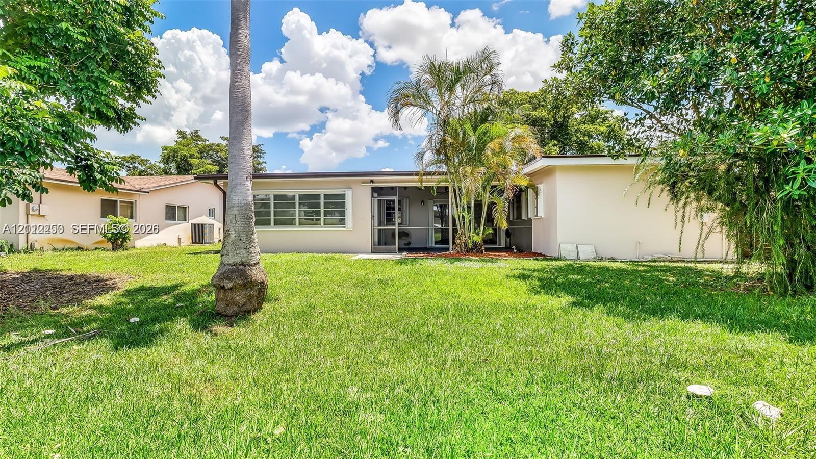 Expansive backyard featuring a large grass lawn, mature palm trees, perimeter foliage, and a screened-in rear patio area