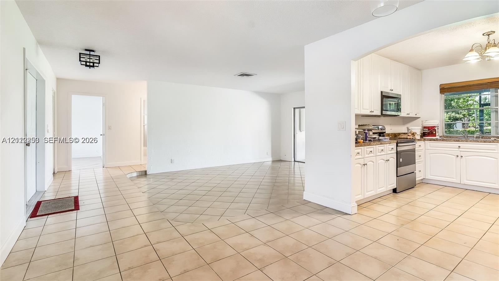 Open-concept interior featuring light-toned tile flooring, white shaker-style cabinetry, stainless steel kitchen appliances, and multi-arm chandelier lighting