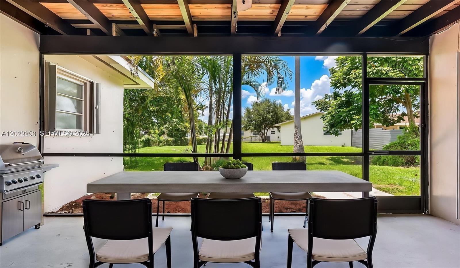Screened-in patio featuring exposed wood-beam ceiling, concrete flooring, and built-in stainless steel outdoor grill